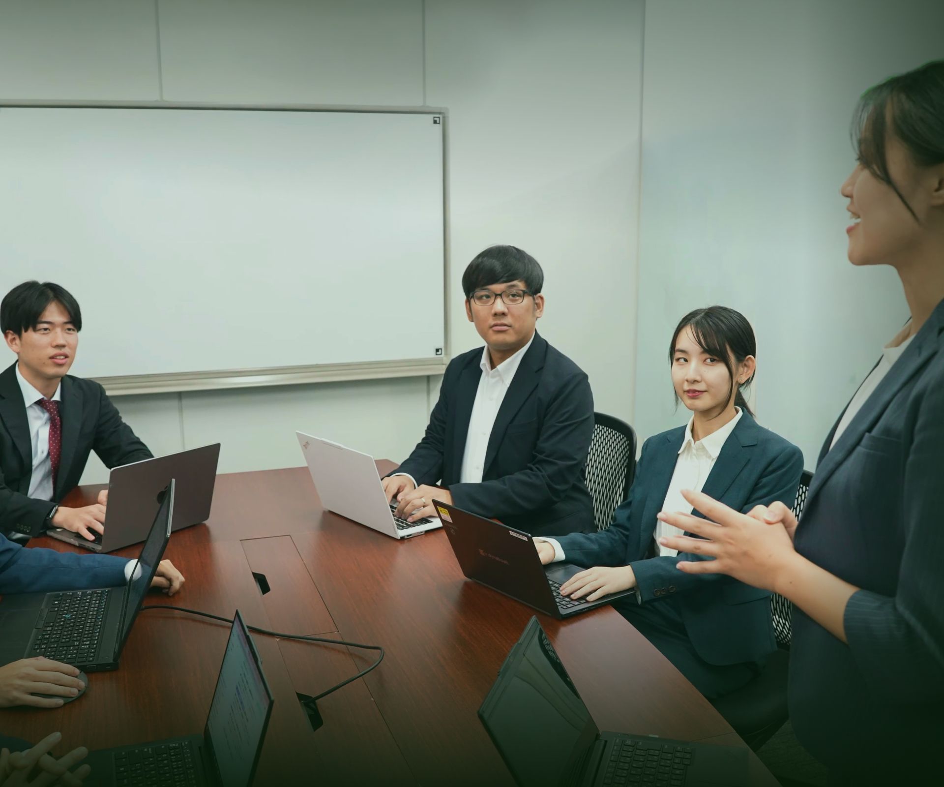 ノートパソコンを開き、会議室で話し合うメンバー